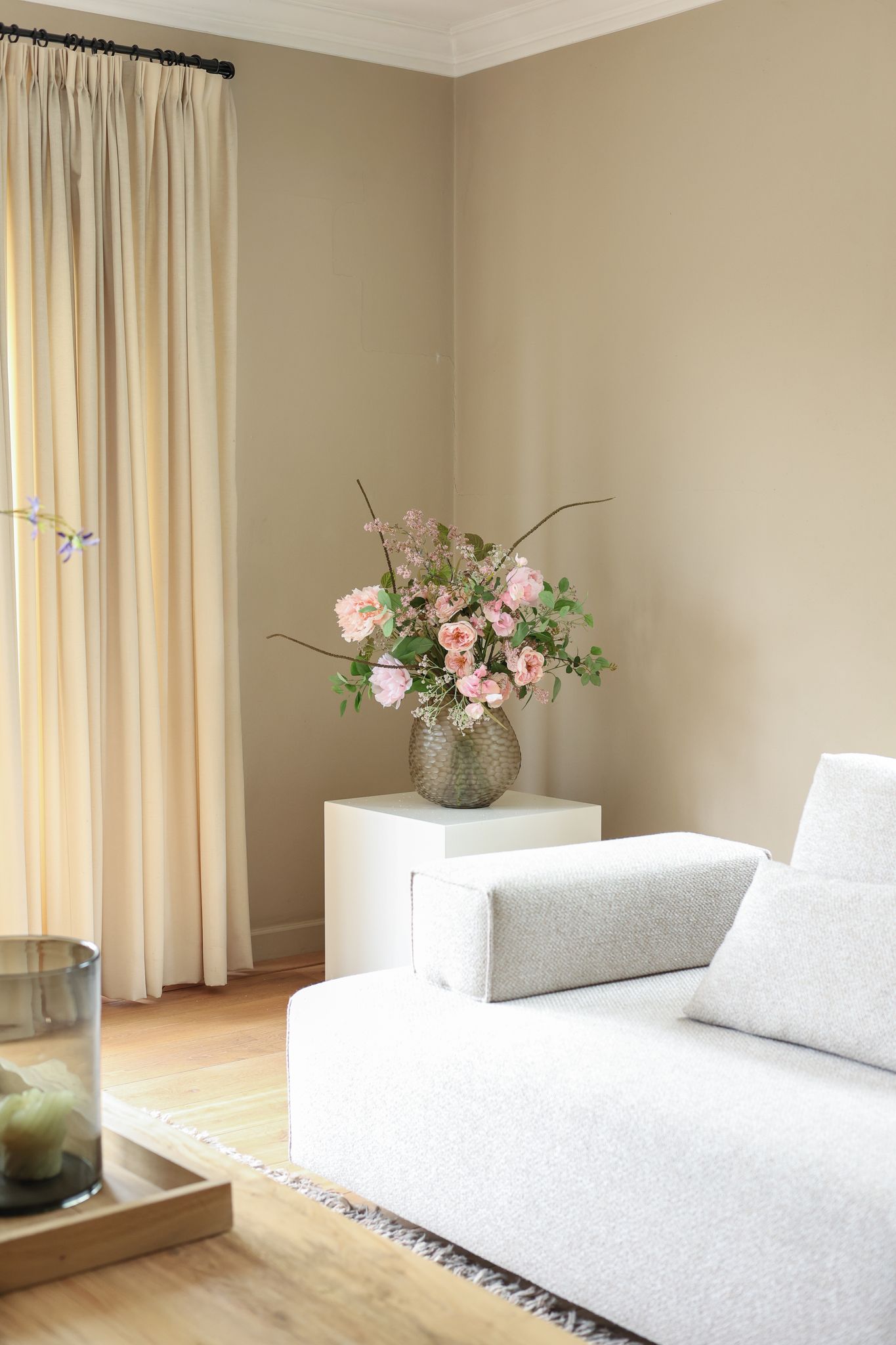 Afstyling aan huis: woonkamer met zijden bloemstuk in een glazen vaas naast een lichte bank