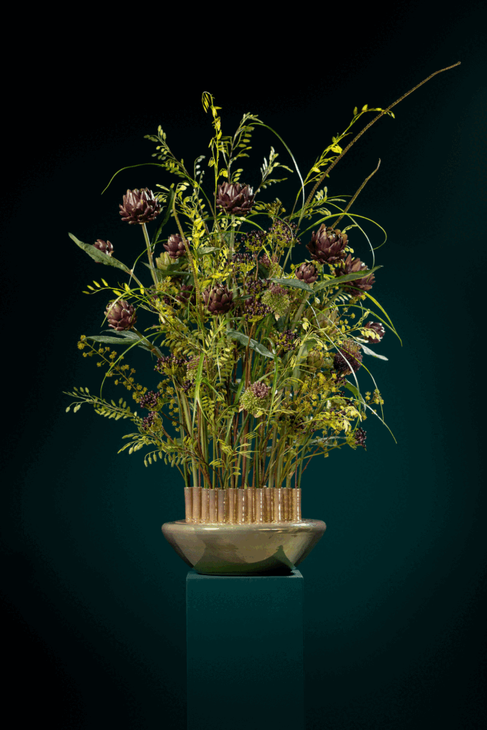 Zijden bloemstuk met artisjokken en grassen in een gouden schaal op een groene zuil