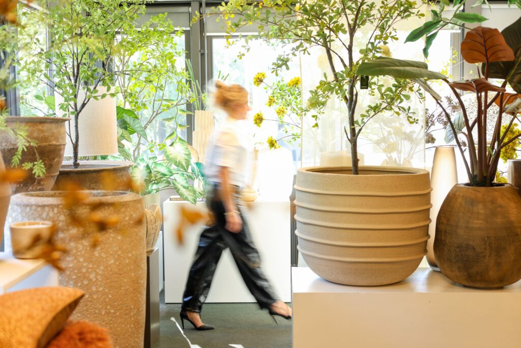 Sophie van Exclusief Ingericht loopt door de lichte winkel tussen potten en kunstbomen