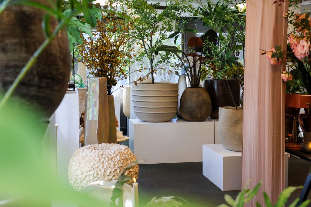 Kunstbomen in grote keramische potten op witte sokkels in de winkel in Oss